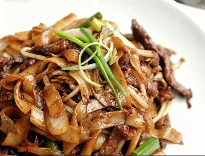 Stir-fried noodles with beef and green onions on a dark plate
