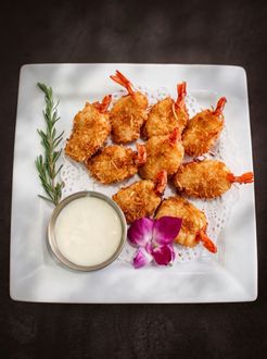 Fried shrimp with dipping sauce on a white plate, garnished with rosemary and a purple flower.