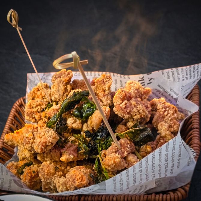 Basket of crispy fried chicken bites garnished with herbs, served in a paper-lined wicker tray.