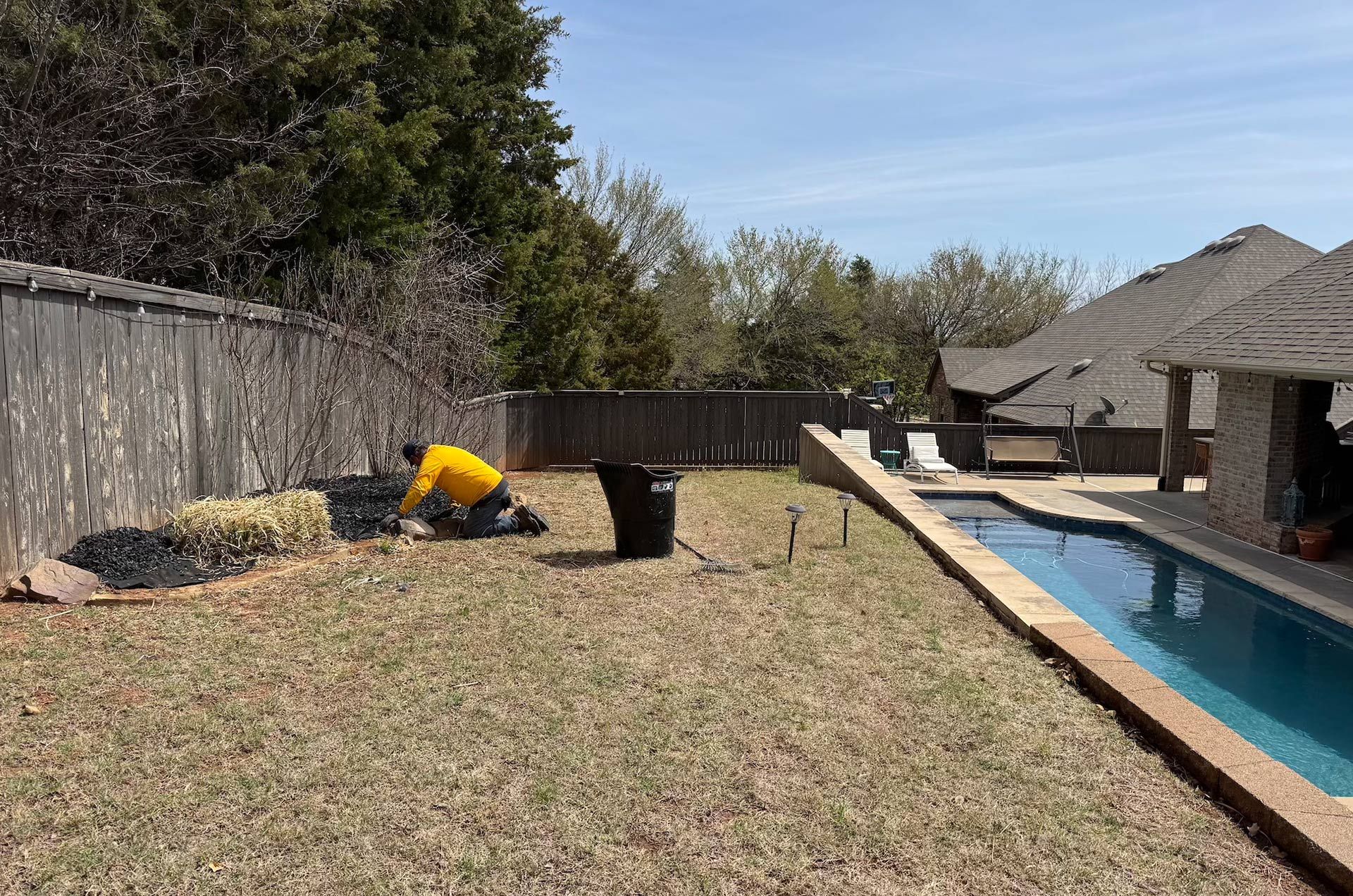 Person tending to plants in a backyard with a pool.