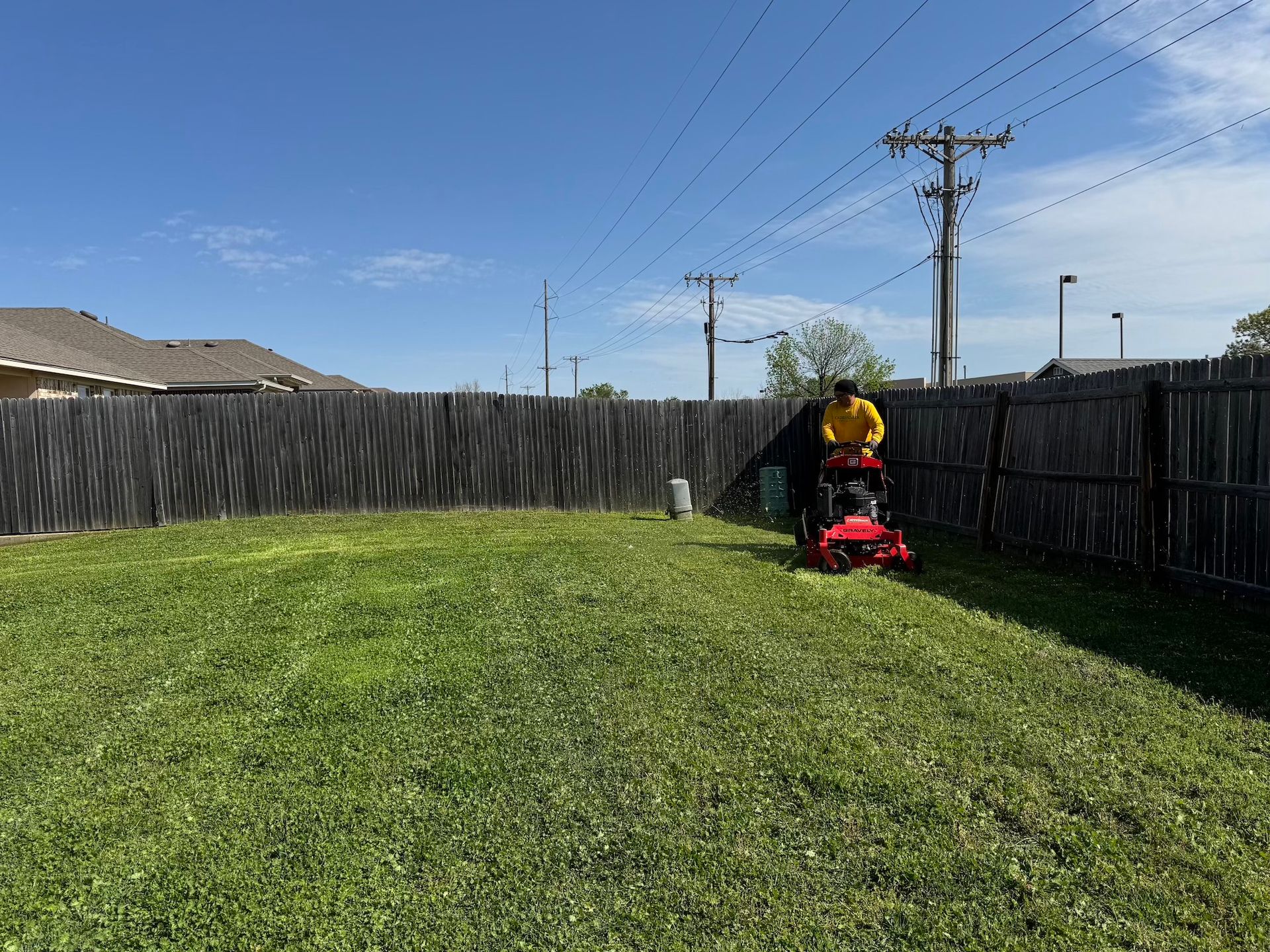 Person mowing a grassy backyard lawn with a red lawnmower on a sunny day.