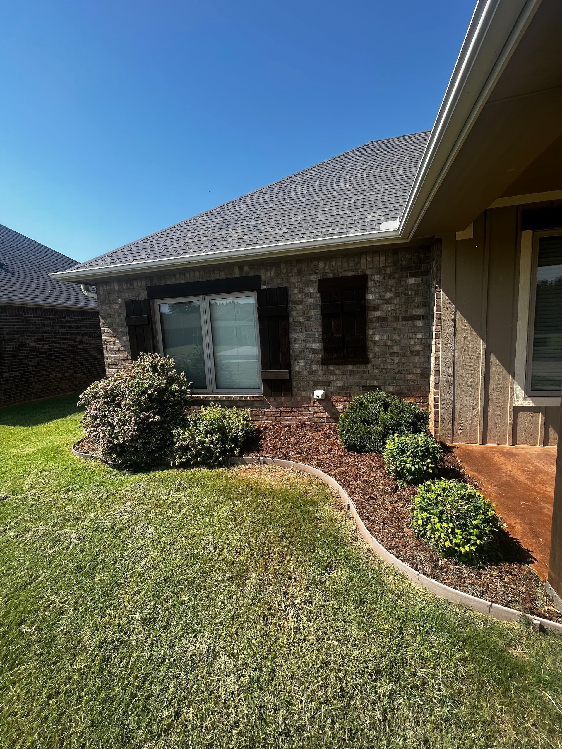 A brick house exterior with a landscaped bed, mulch, green grass, and blue sky.