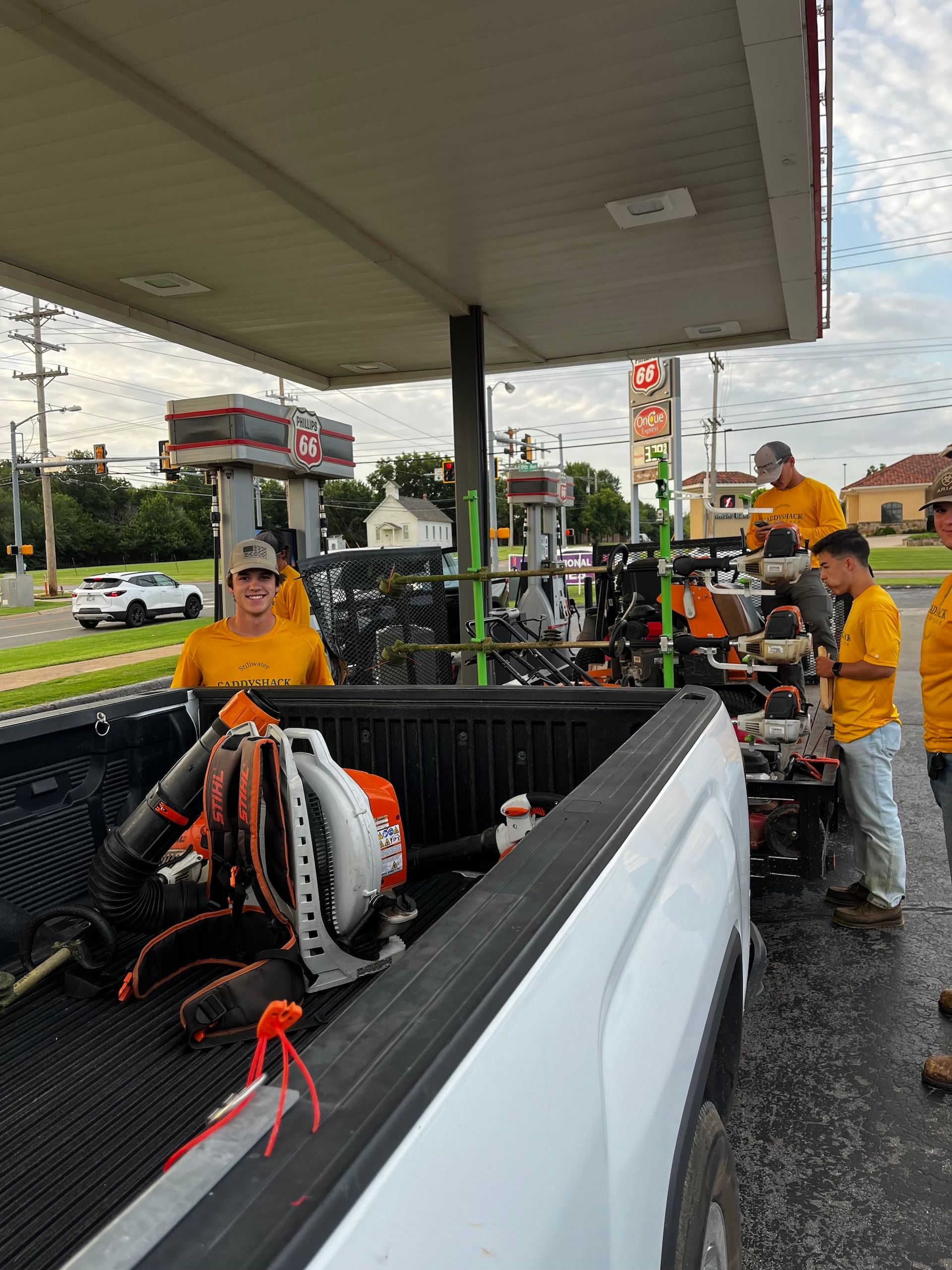 Landscaping crew at a gas station, fueling a truck. They wear yellow shirts.