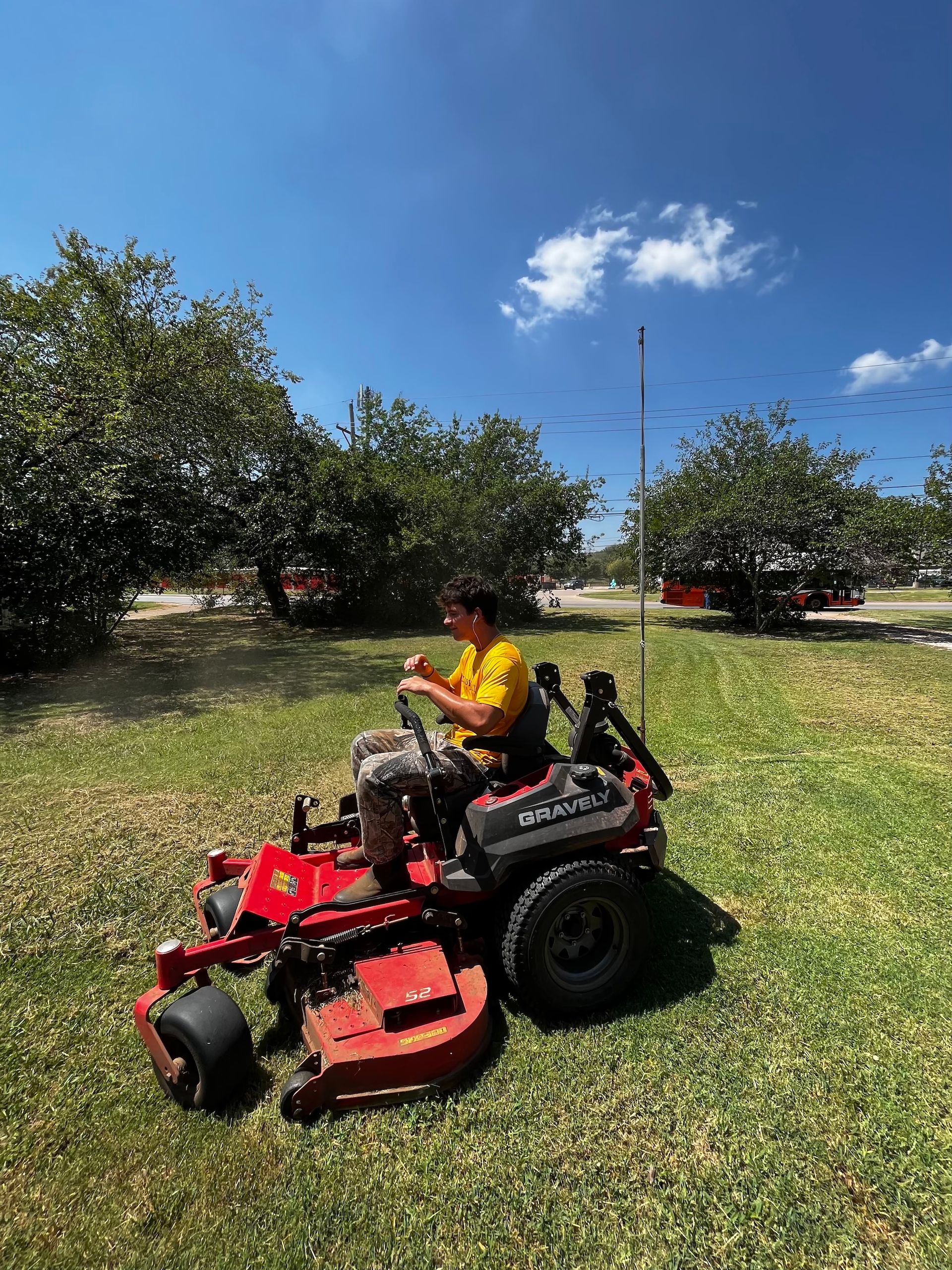Person on a red zero-turn mower cutting grass on a sunny day.