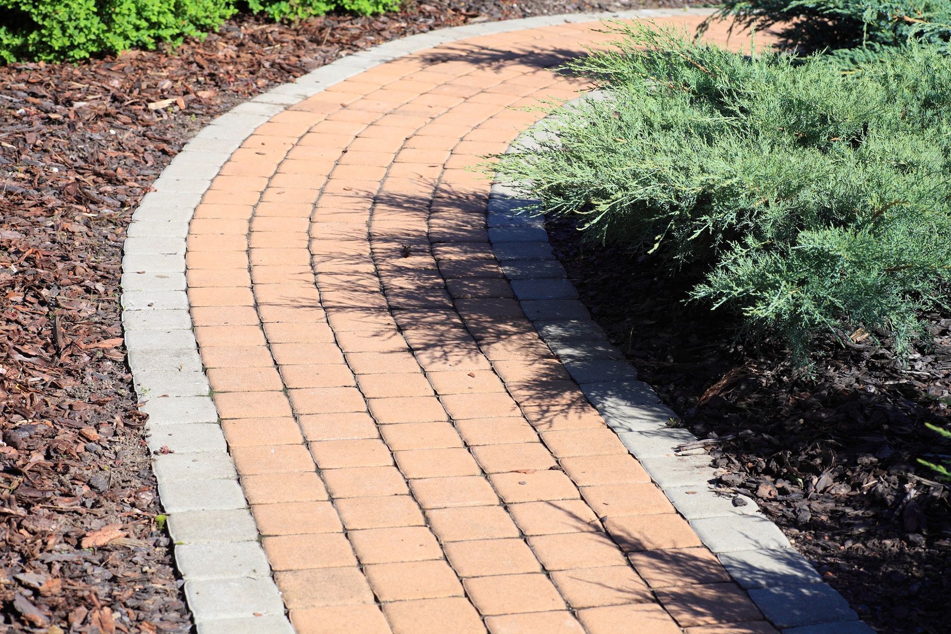 Curving brick pathway with a light border, next to green bushes.