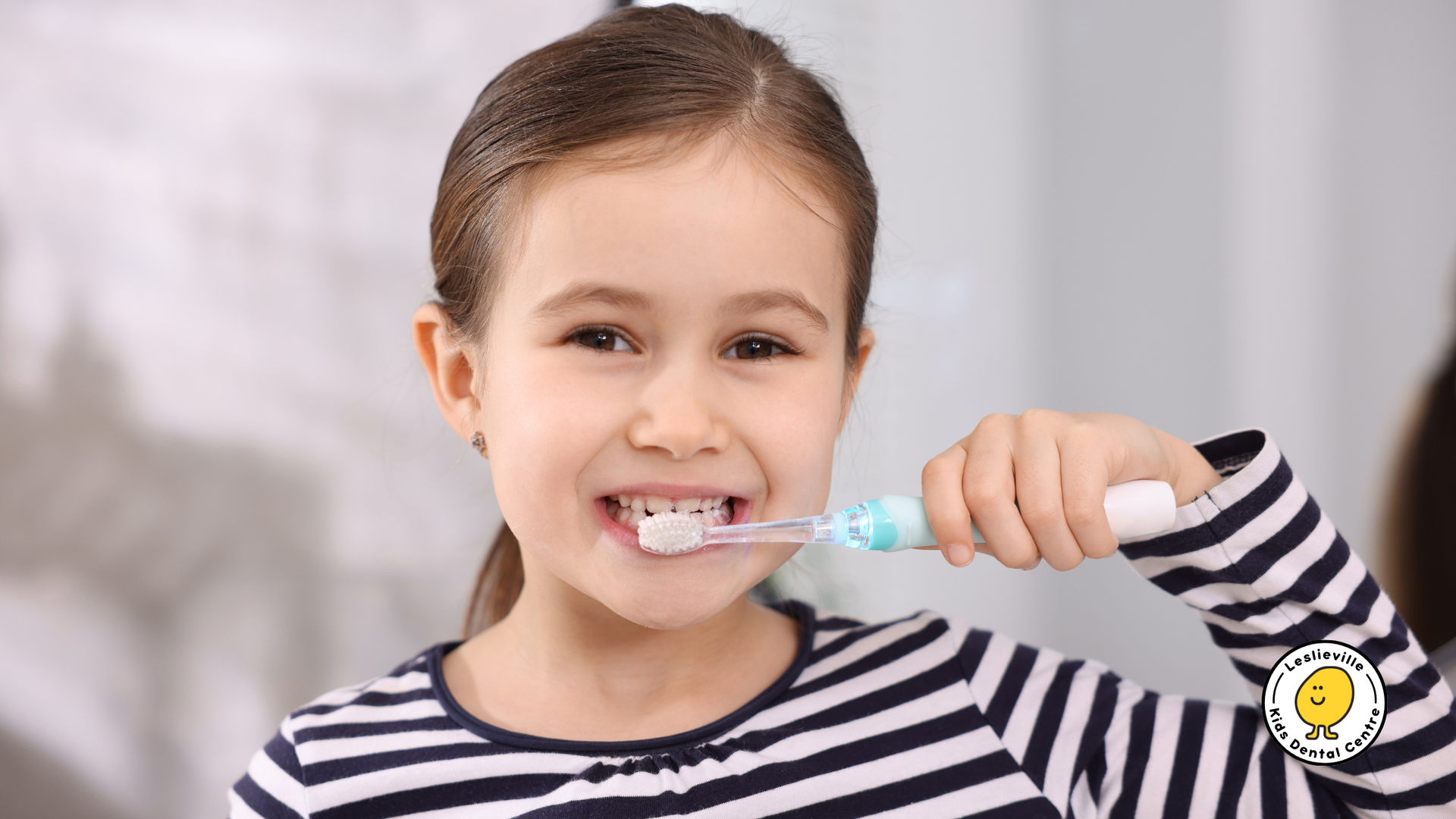 Girl smiling while brushing her teeth with an electric toothbrush in front of a mirror.