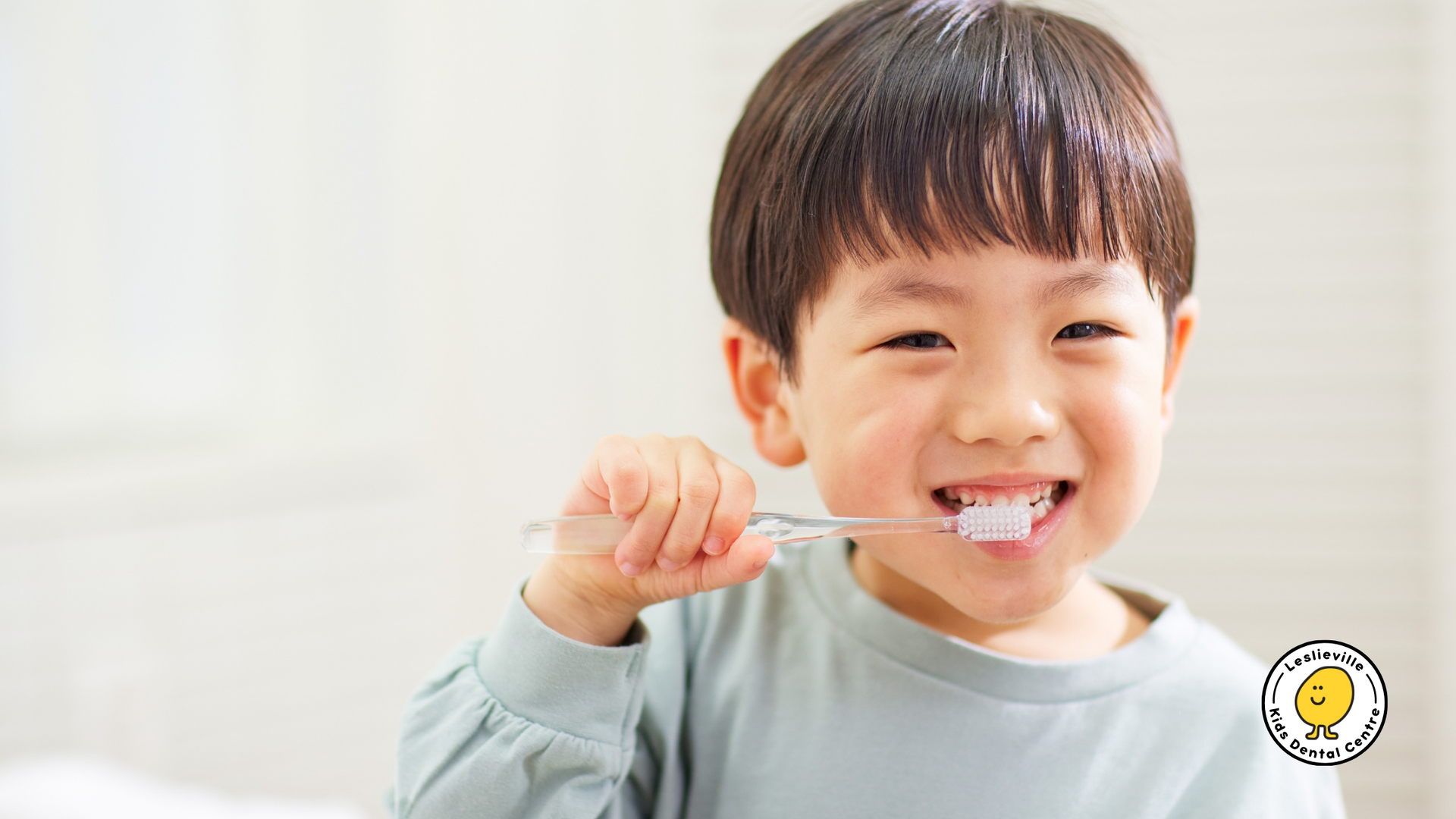 Boy brushing teeth, smiling. Light blue shirt, clear toothbrush.