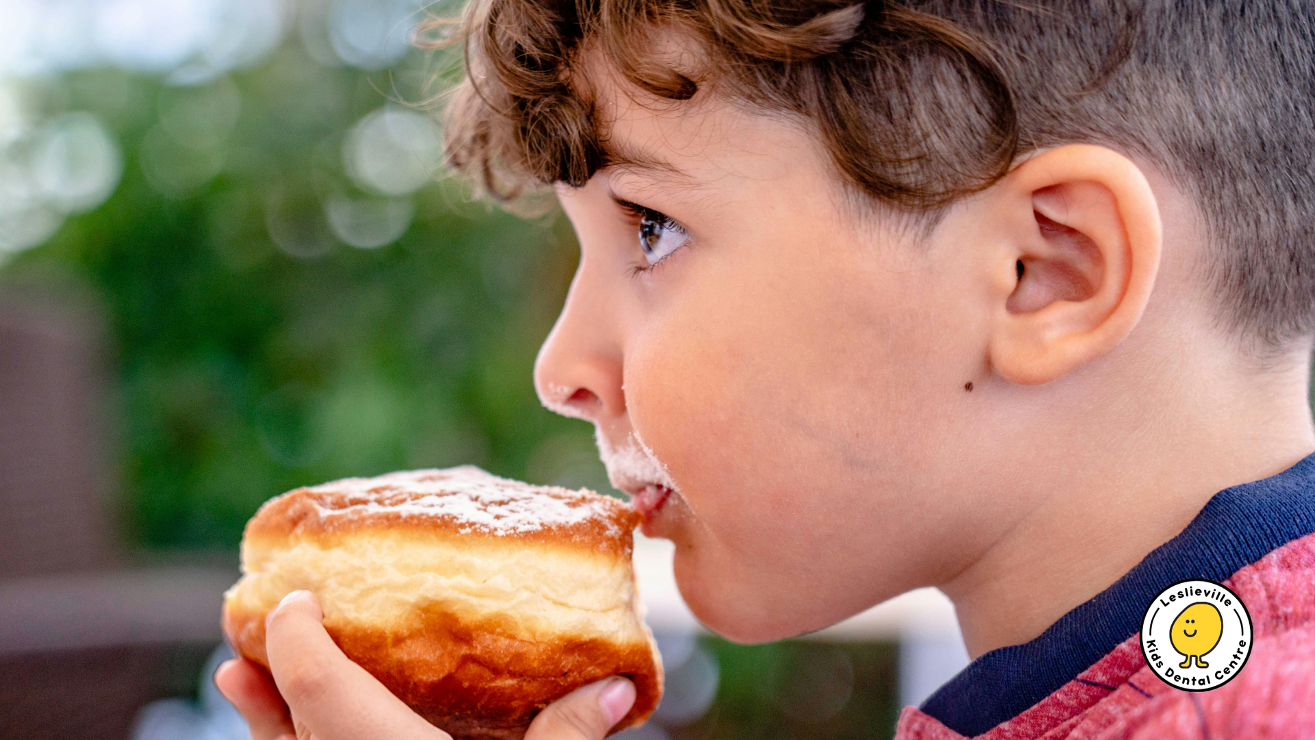 Boy eating a powdered-sugar-covered donut outdoors, close-up.