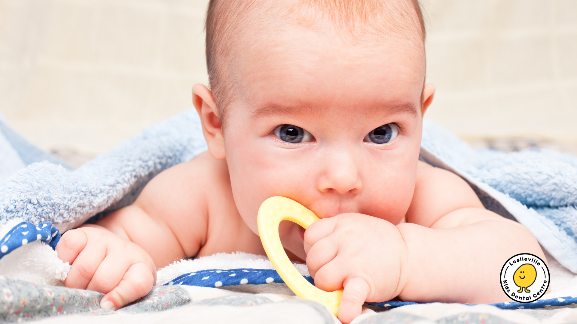 A baby is chewing on a yellow teething ring while laying on a blanket.