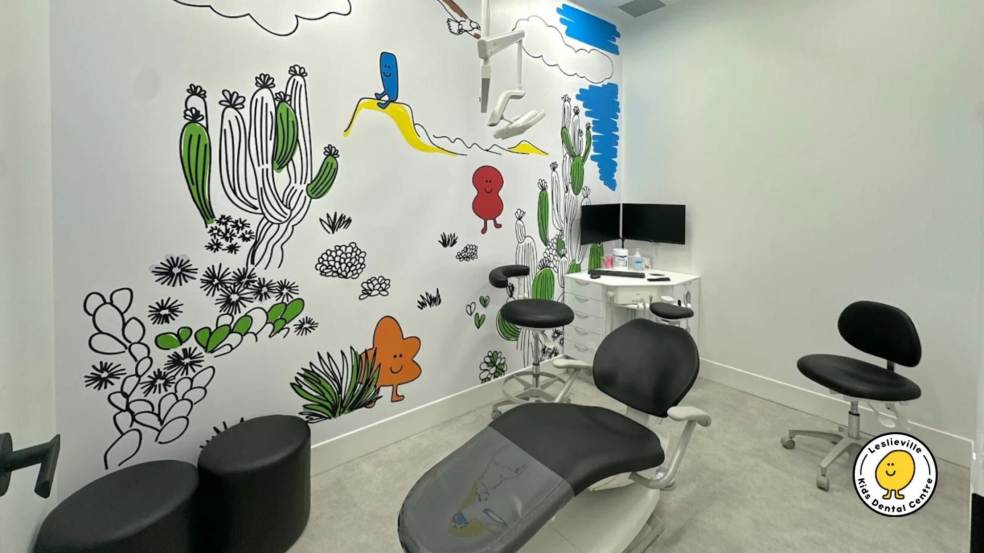 A pediatric dental exam room with a whimsical desert-themed wall mural, a dental chair, and small stools.
