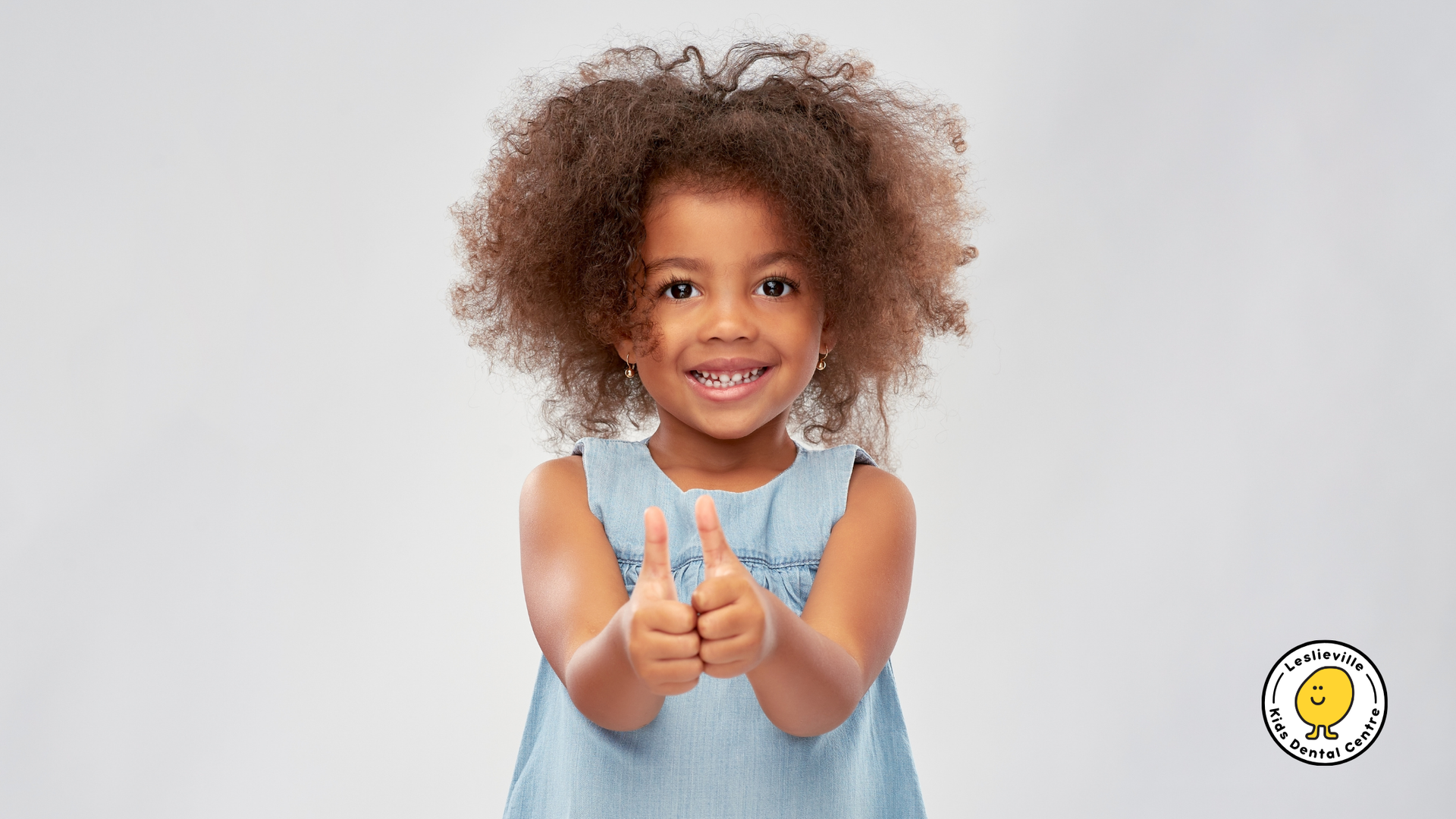 Smiling child with curly hair giving a thumbs-up.