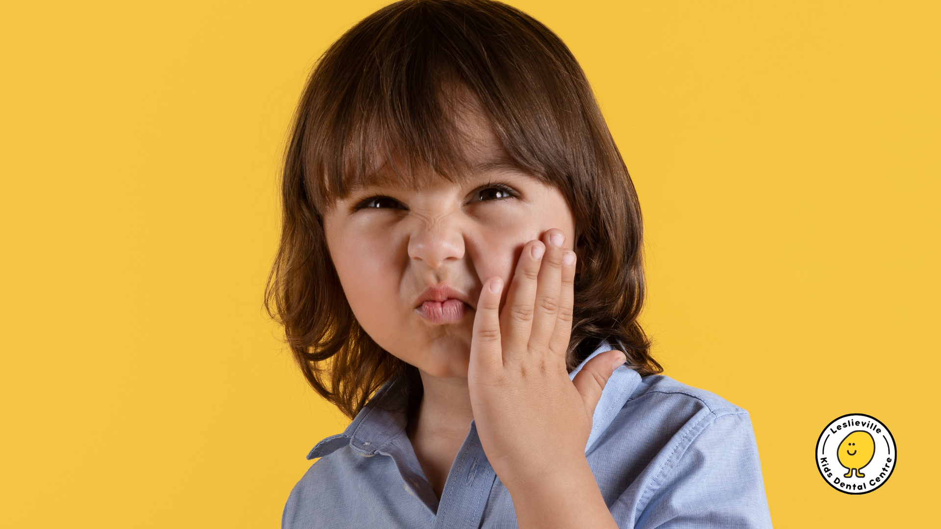 A young boy is making a funny face with his hand on his face.