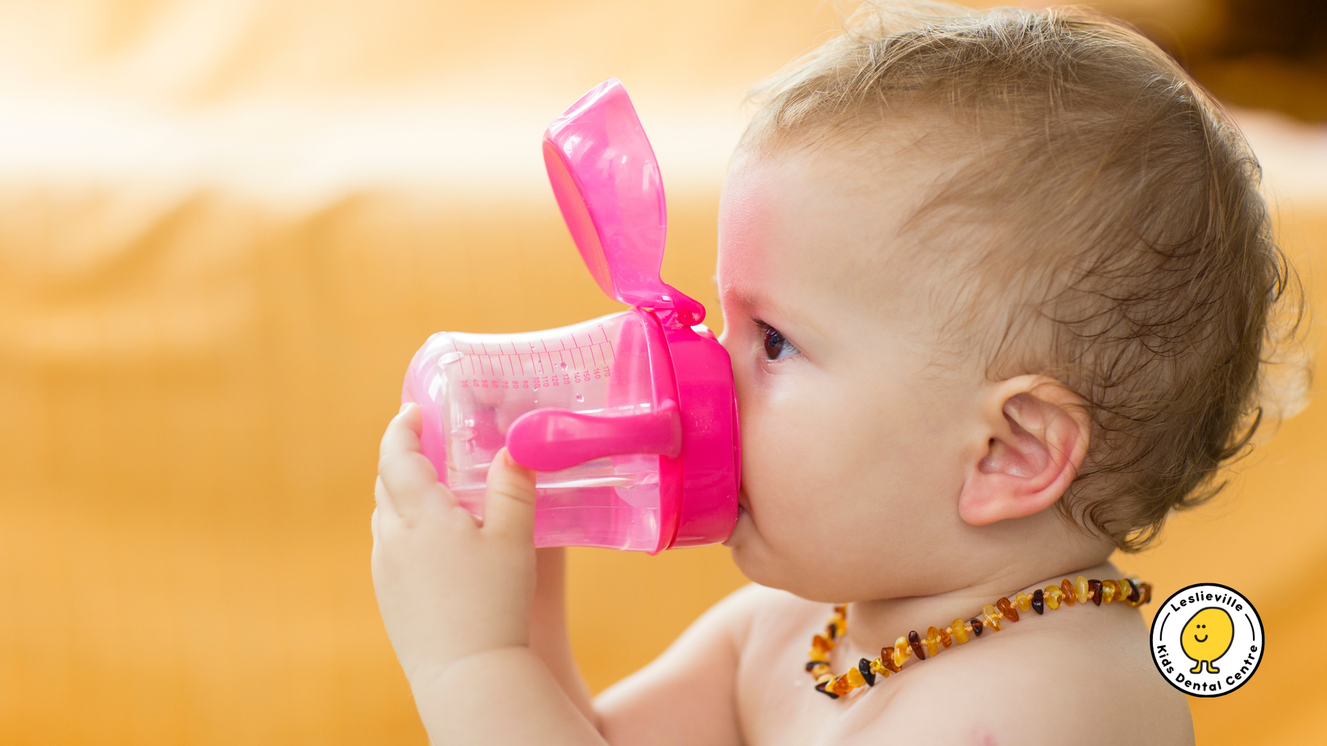 A baby is drinking from a pink cup with a straw.
