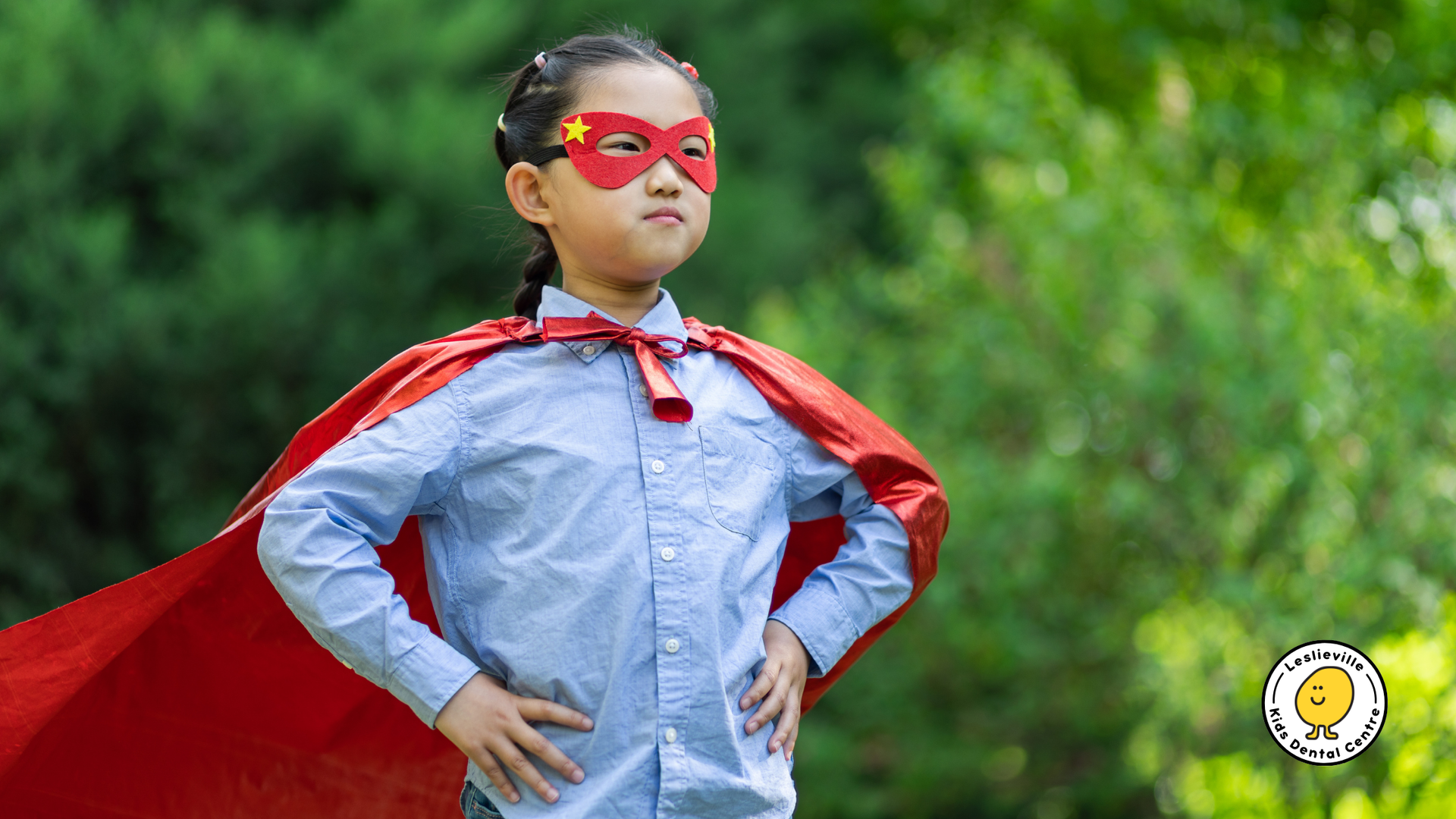 A child wears a superhero cape and a mask featuring a gold star, standing confidently with hands on hips in a garden.