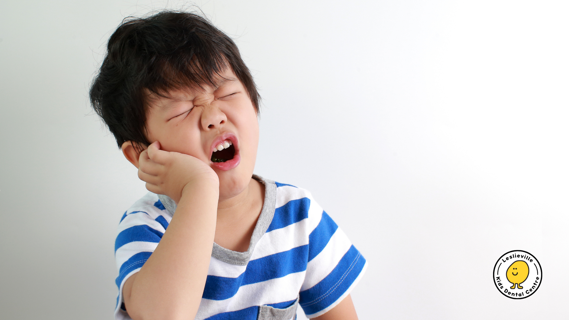 A young boy in a blue and white striped shirt is yawning.