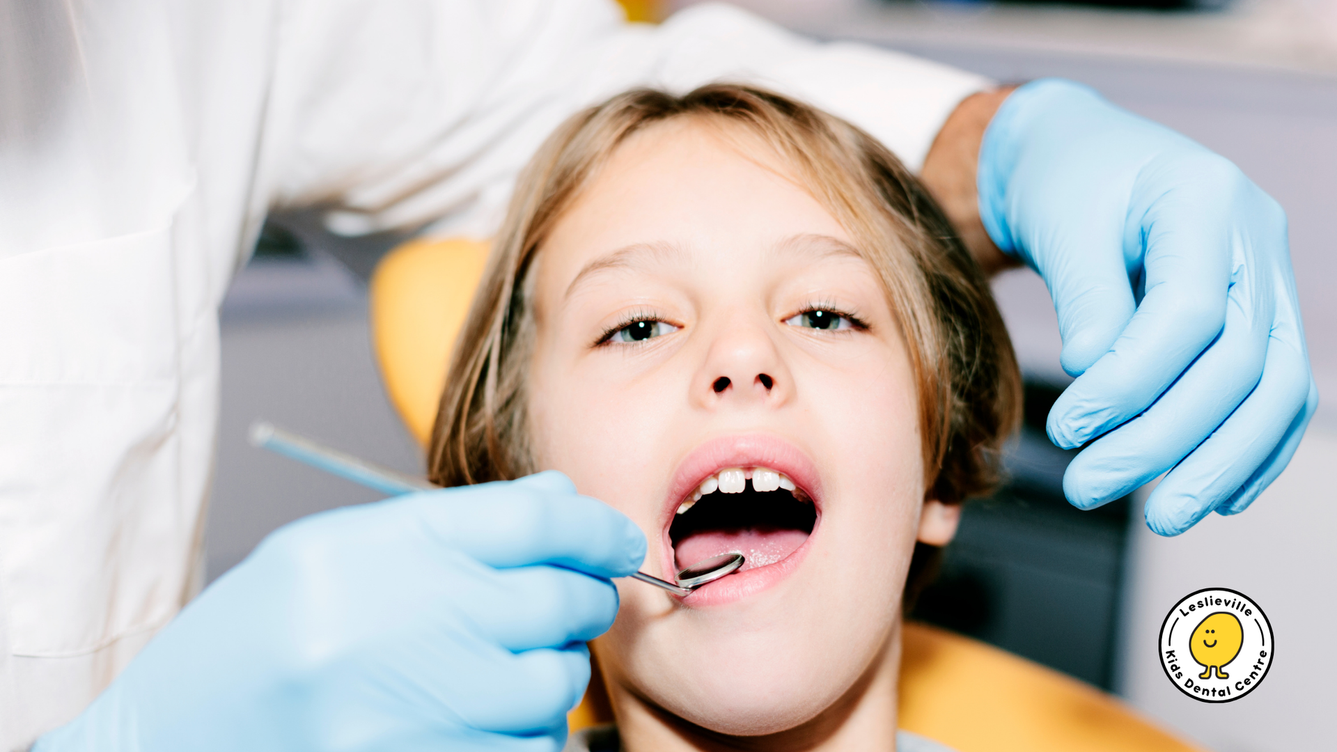 Child at dentist with mouth open, dental tools, and gloved hands.