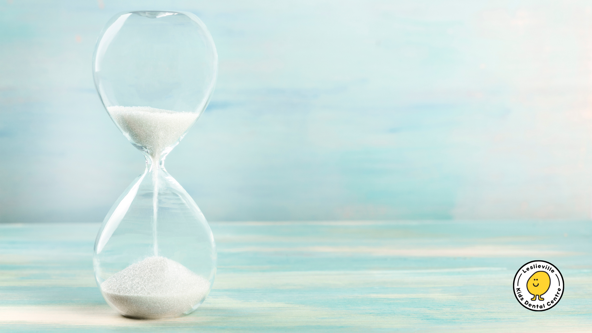 Hourglass with white sand on a light blue wooden surface.