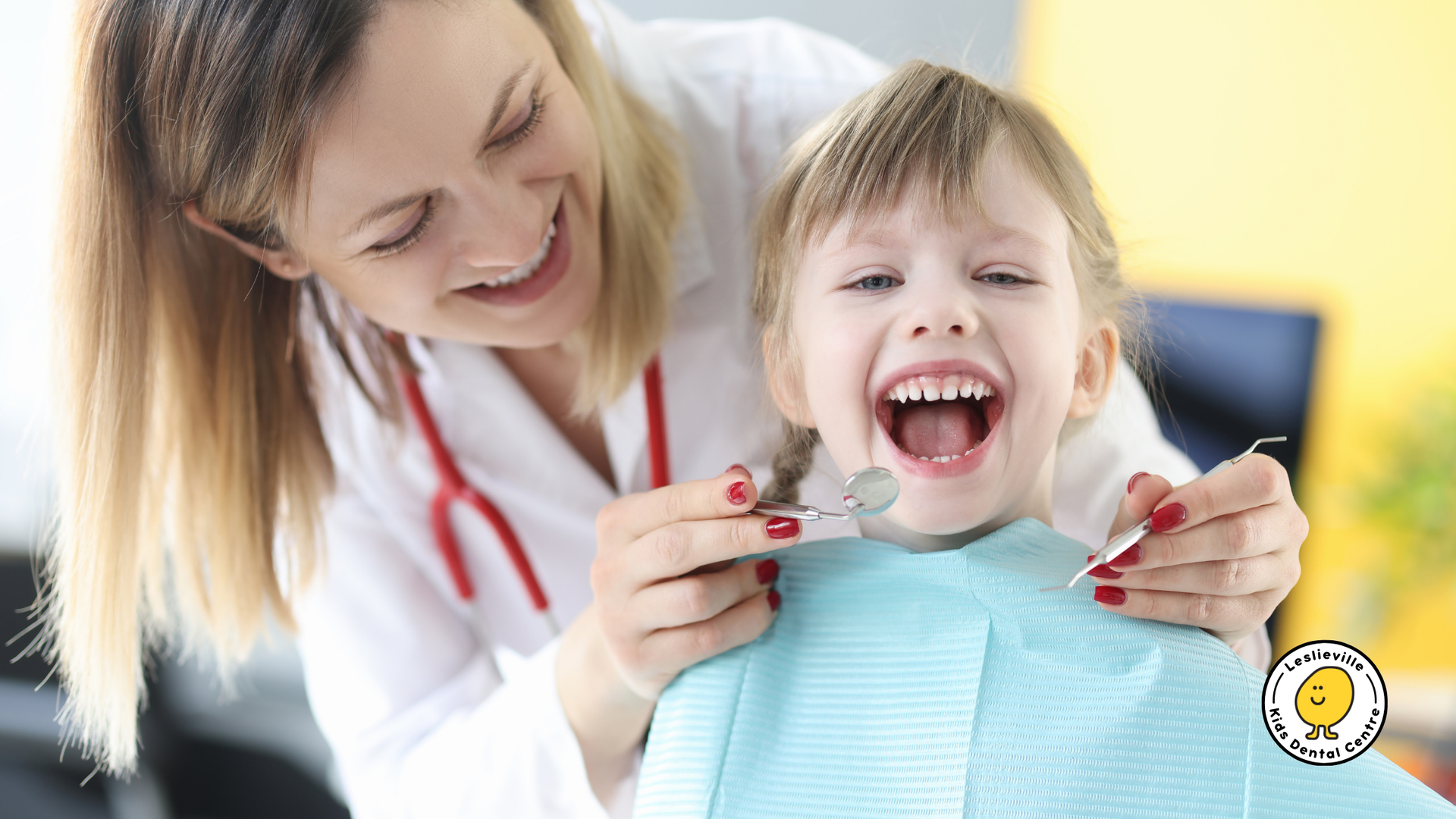 A smiling dentist holding a dental mirror examines a young patient’s teeth.