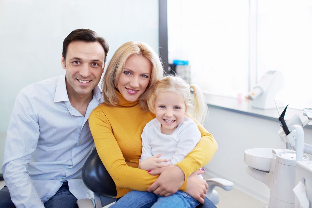 A smiling family of three posing together in a bright, modern dental office.