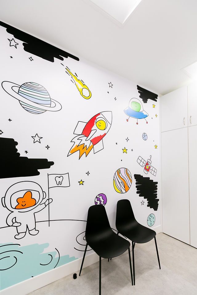 A wall mural of space exploration in a room with two black chairs against a white cabinet.