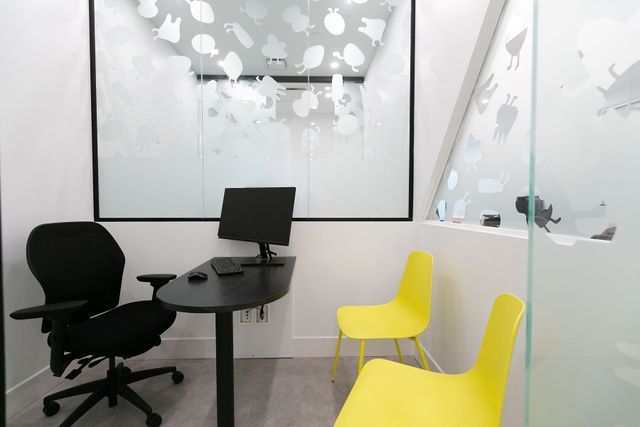 A modern office room with a dark desk, an ergonomic black chair, and two bright yellow chairs against white walls.