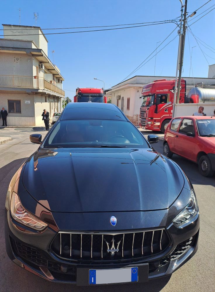 Una Maserati nera parcheggiata in una strada con autopompe e edifici sullo sfondo.