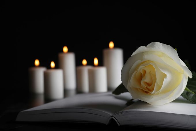 Una rosa bianca su un libro aperto con candele accese sullo sfondo, contro uno sfondo scuro.