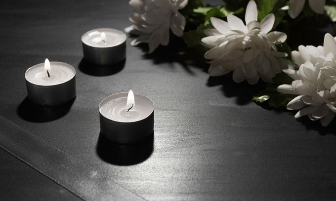 Tre candele tealight accese su una superficie scura accanto a fiori bianchi
