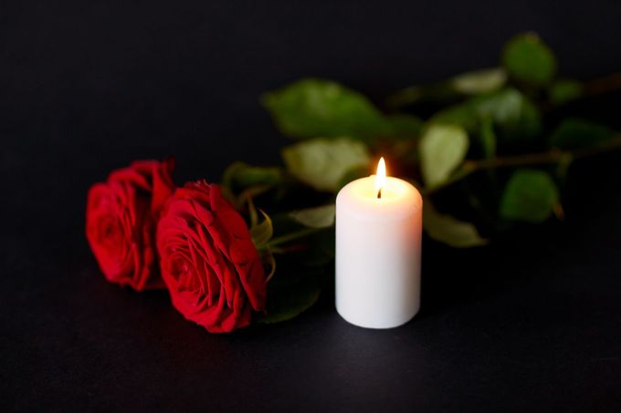 Due rose rosse e una candela bianca accesa su uno sfondo scuro