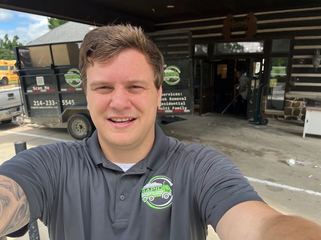 Selfie of a smiling person in a gray polo shirt standing outside a service shop with a truck behind them