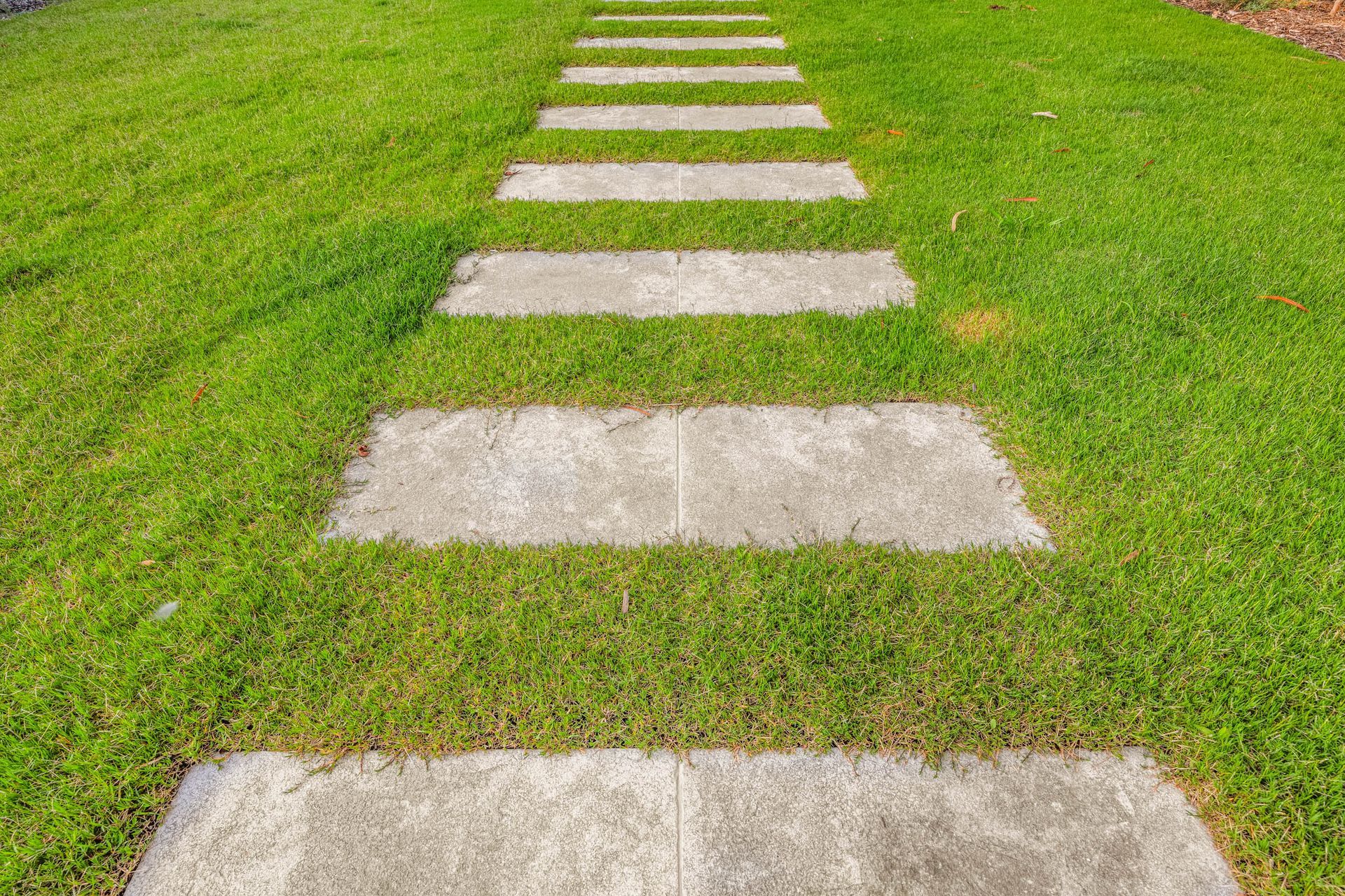 A stone paver pathway leading through a vibrant green lawn.
