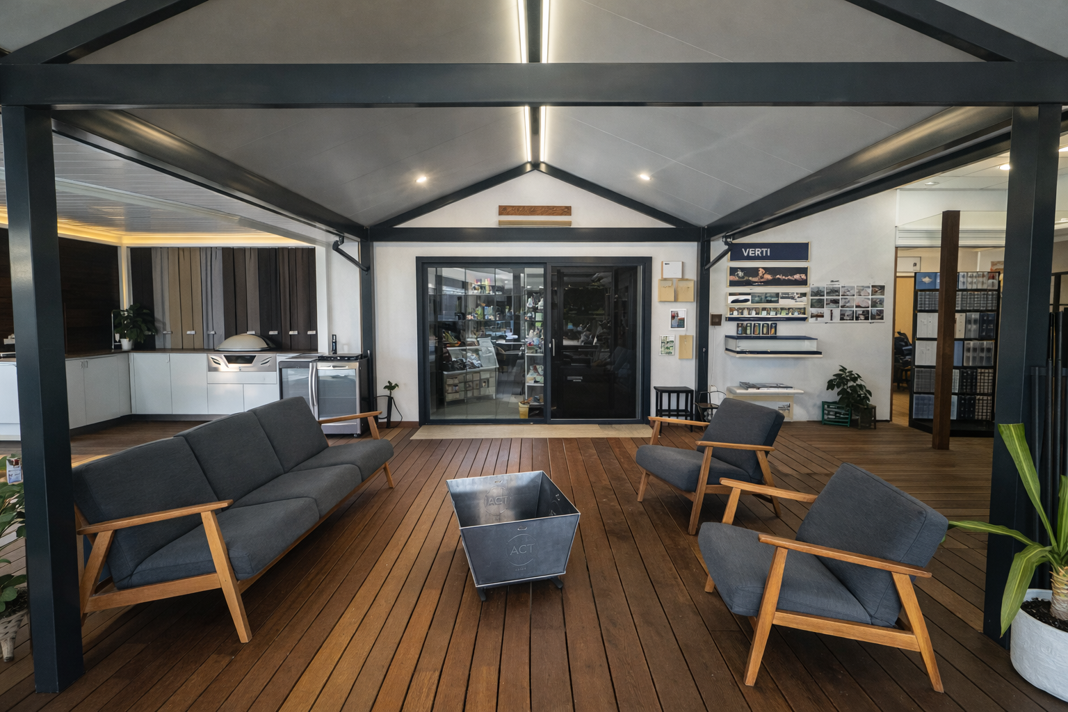 A covered outdoor lounge area featuring a grey sofa, two matching armchairs, and a metal fire pit on a wooden deck.