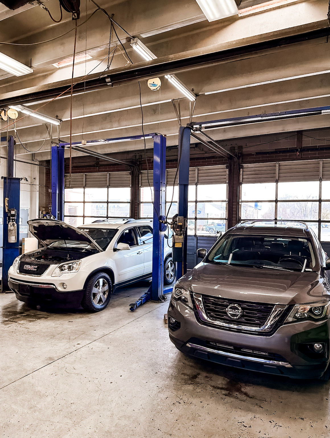 Two cars inside an auto repair garage, one on a lift and one parked in front.