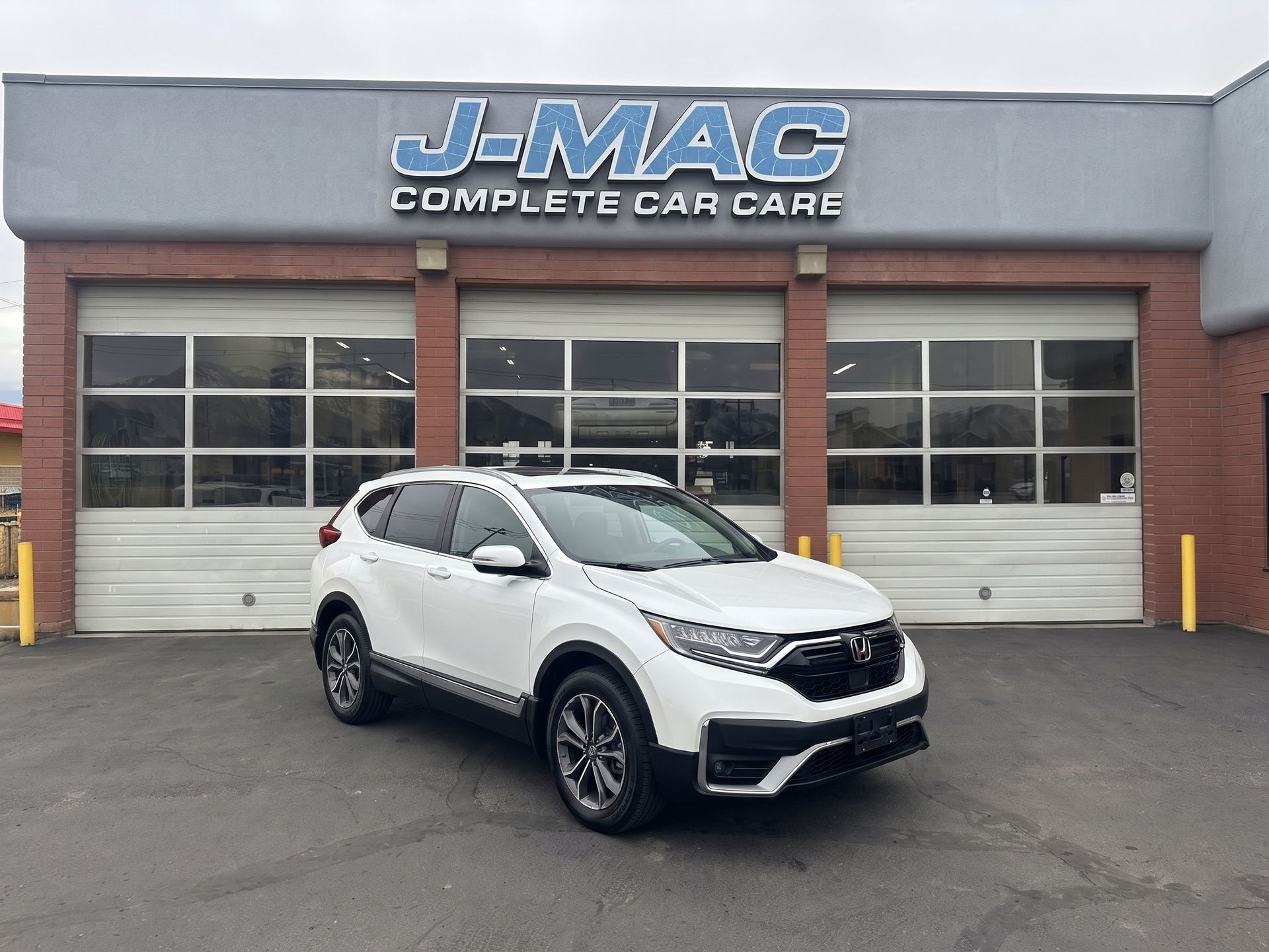 White SUV parked outside J-MAC Complete Car Care garage with closed bay doors.