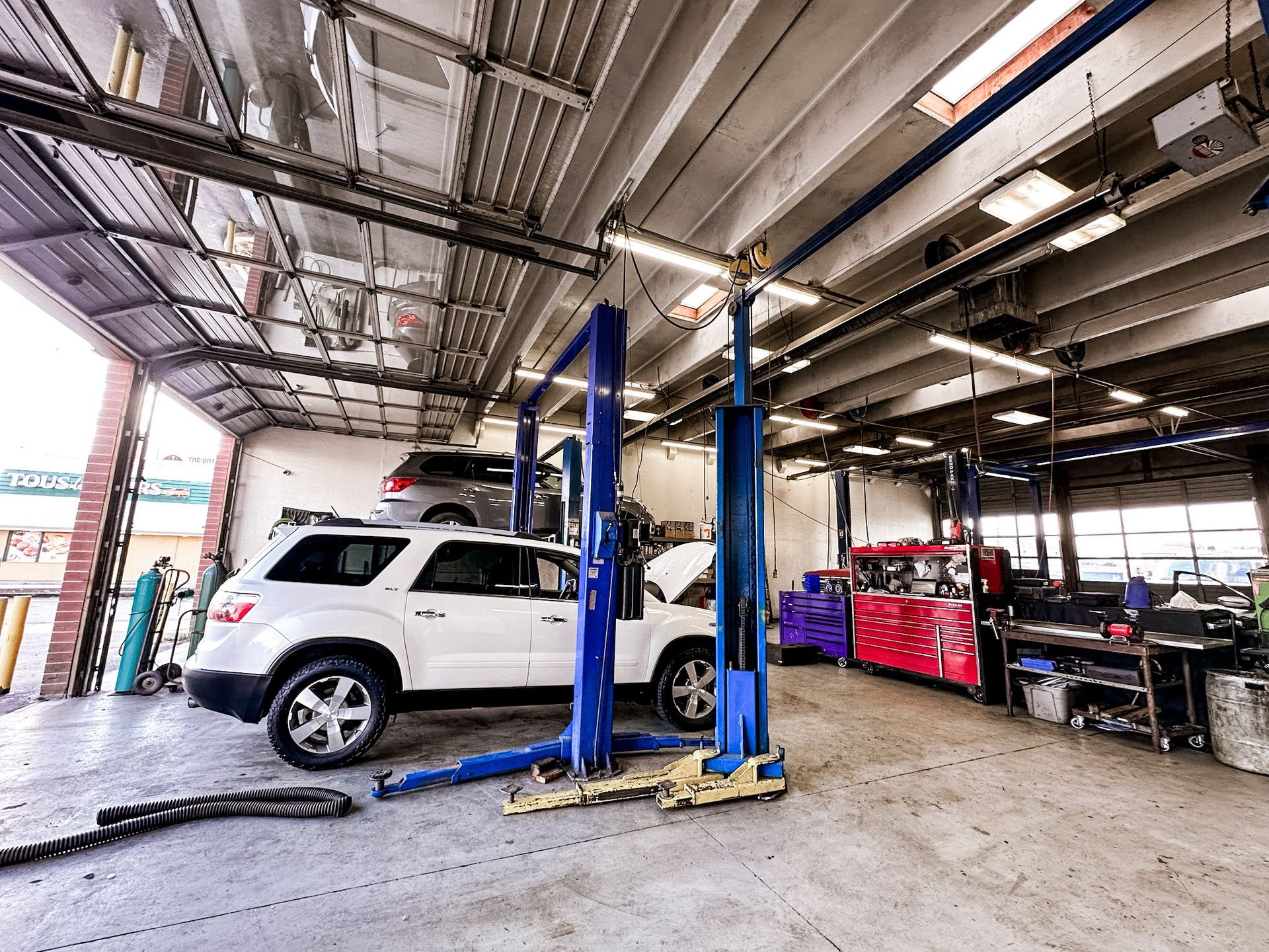 Auto repair shop with a white SUV on a lift and tools in a bright garage