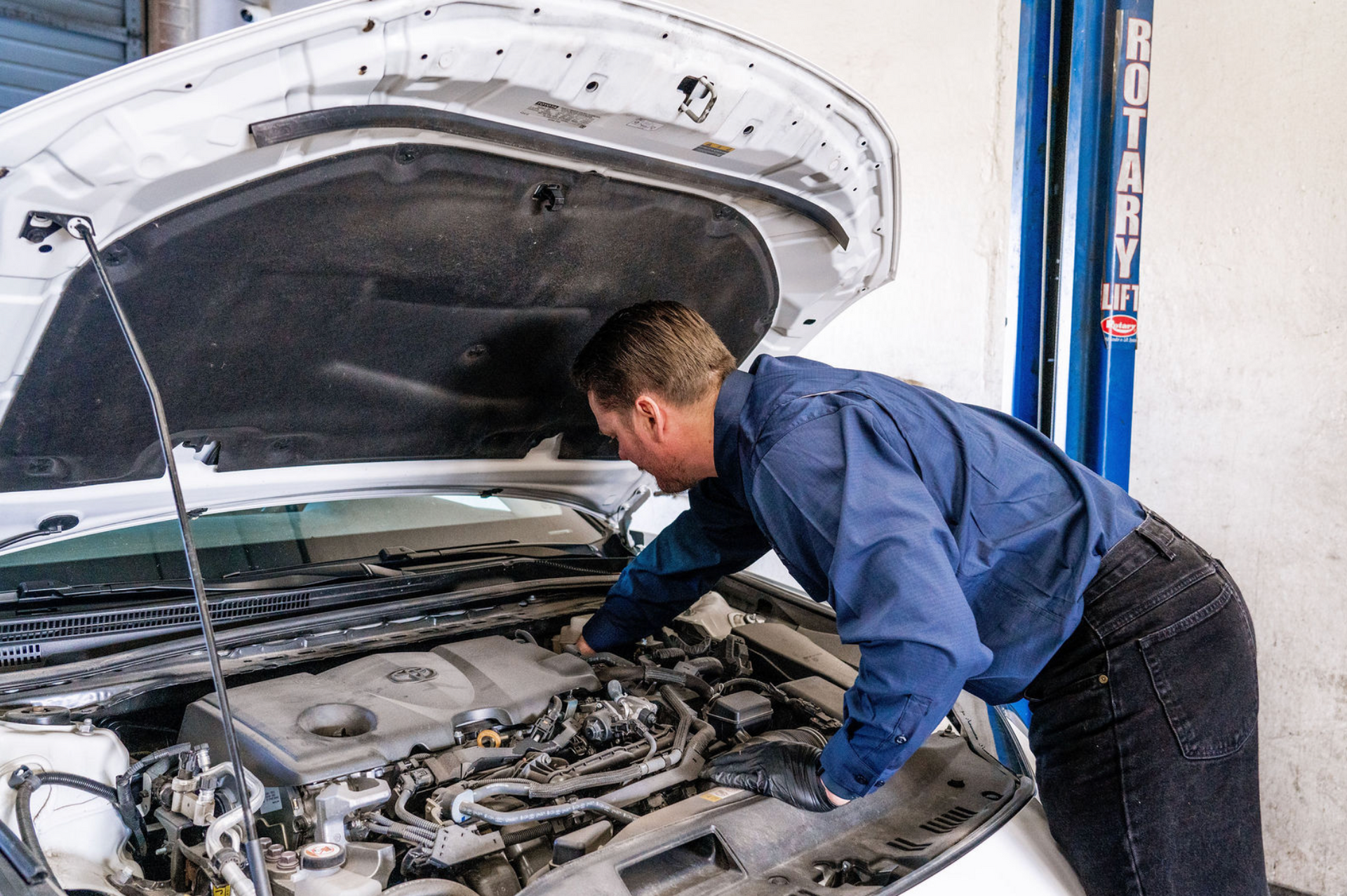 Mechanic inspecting a car engine with the hood open in a garage