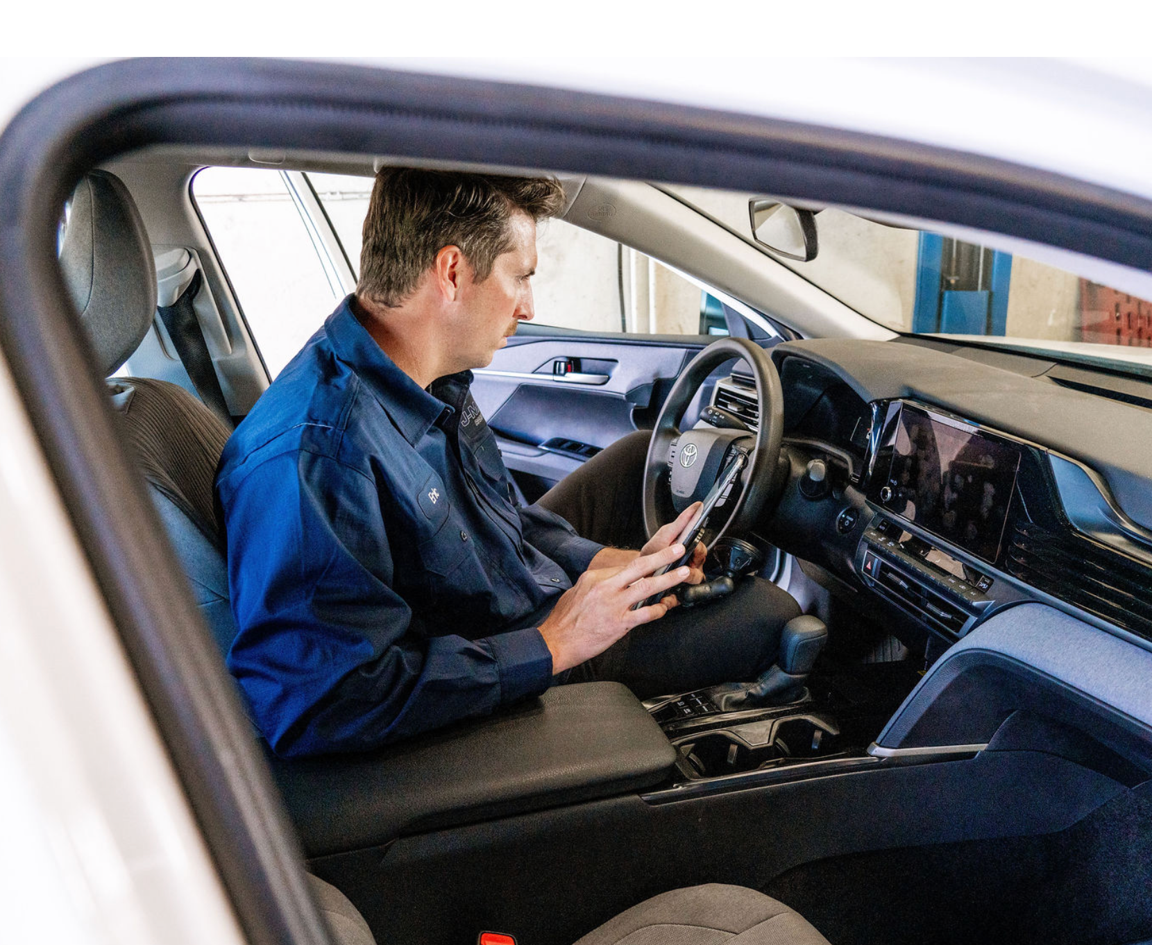 Man sitting in a car driver’s seat, looking at the dashboard and holding a phone.