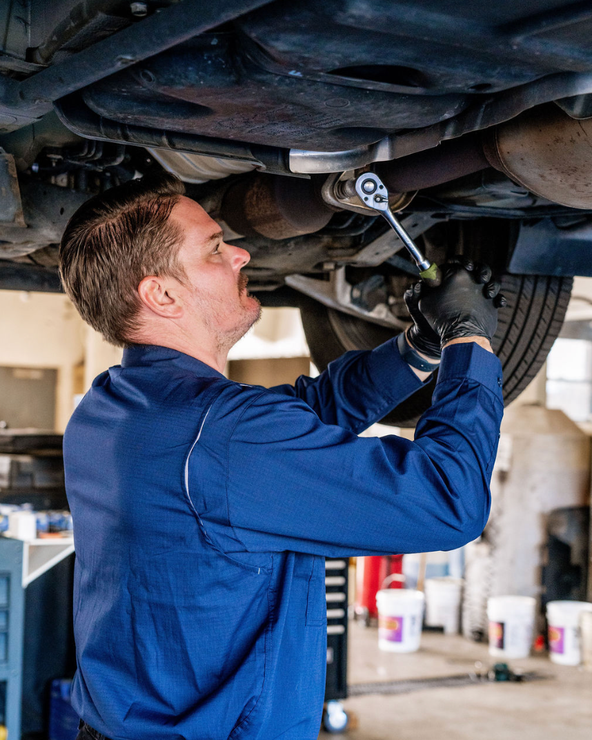 Mechanic in blue coveralls tightening bolts under a lifted car in a garage