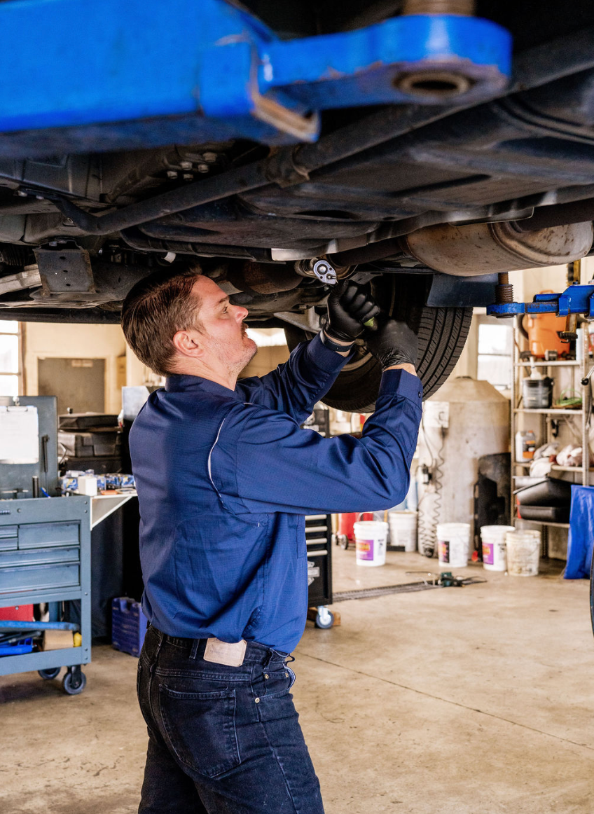 Mechanic in blue shirt working under a lifted car in a garage