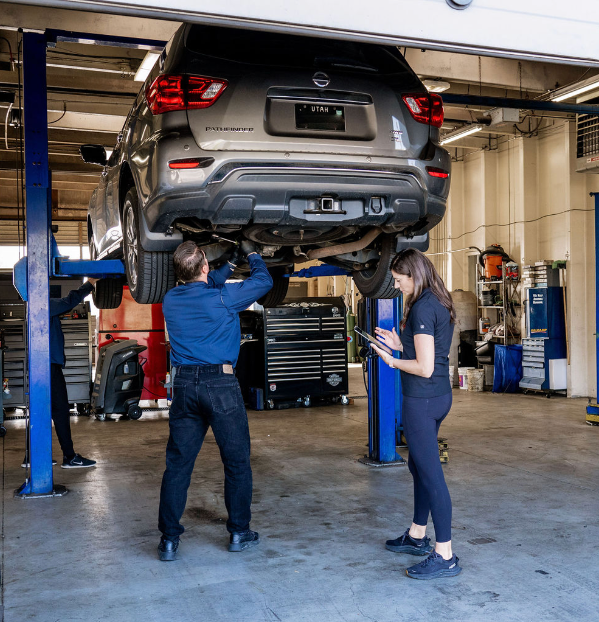 Mechanics inspecting a car lifted on a repair hoist in an auto shop
