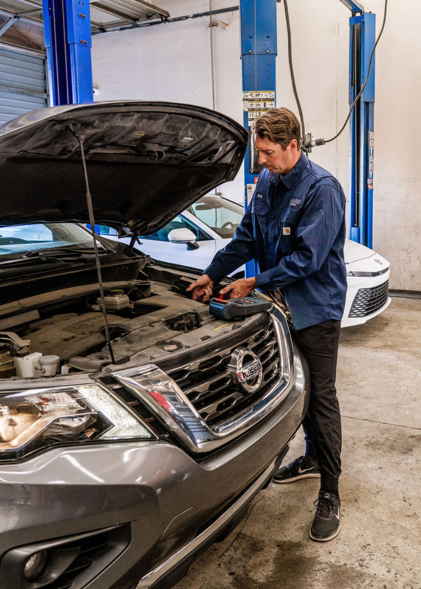 Mechanic inspecting a silver SUV with hood open in an auto repair shop