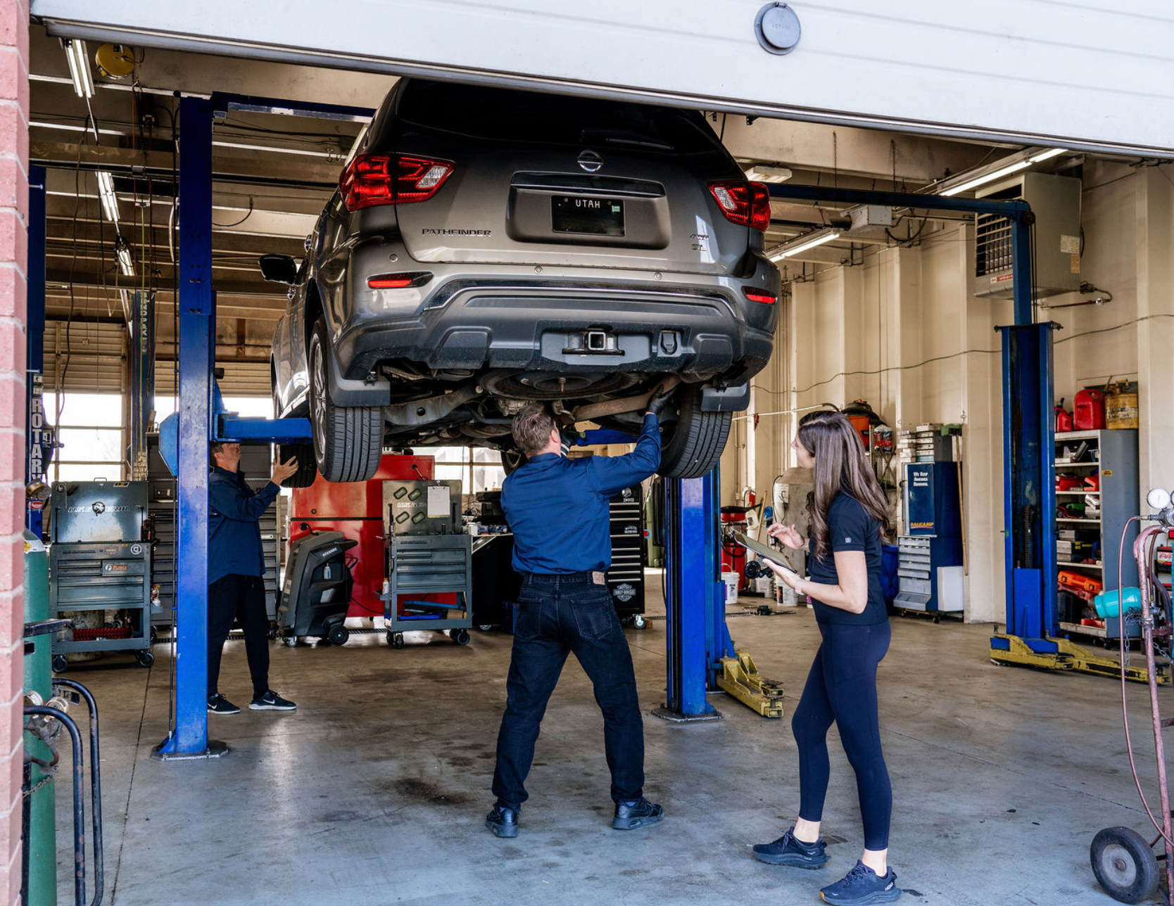 Mechanic inspecting a gray SUV lifted on a car repair lift in an auto shop