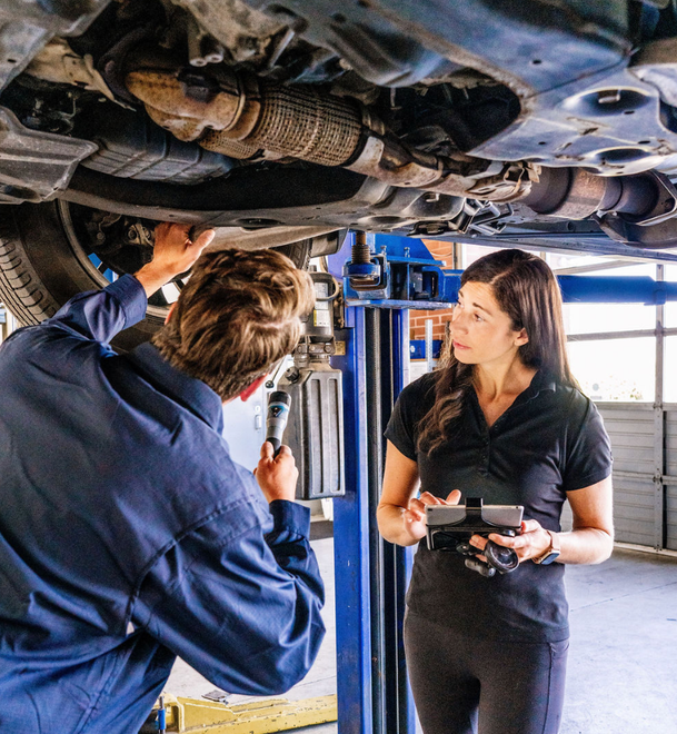 Two mechanics inspecting a car’s undercarriage on a lift in a garage.