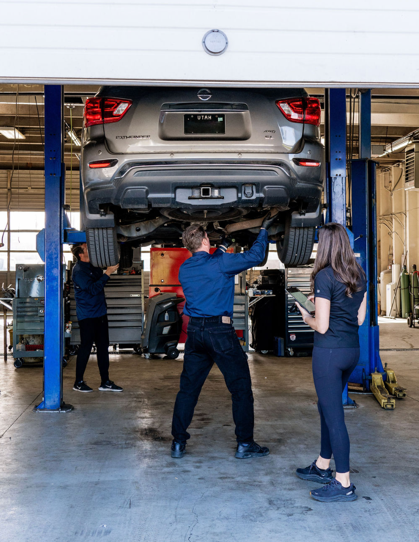 Car lifted in auto repair bay with three mechanics working underneath and around it