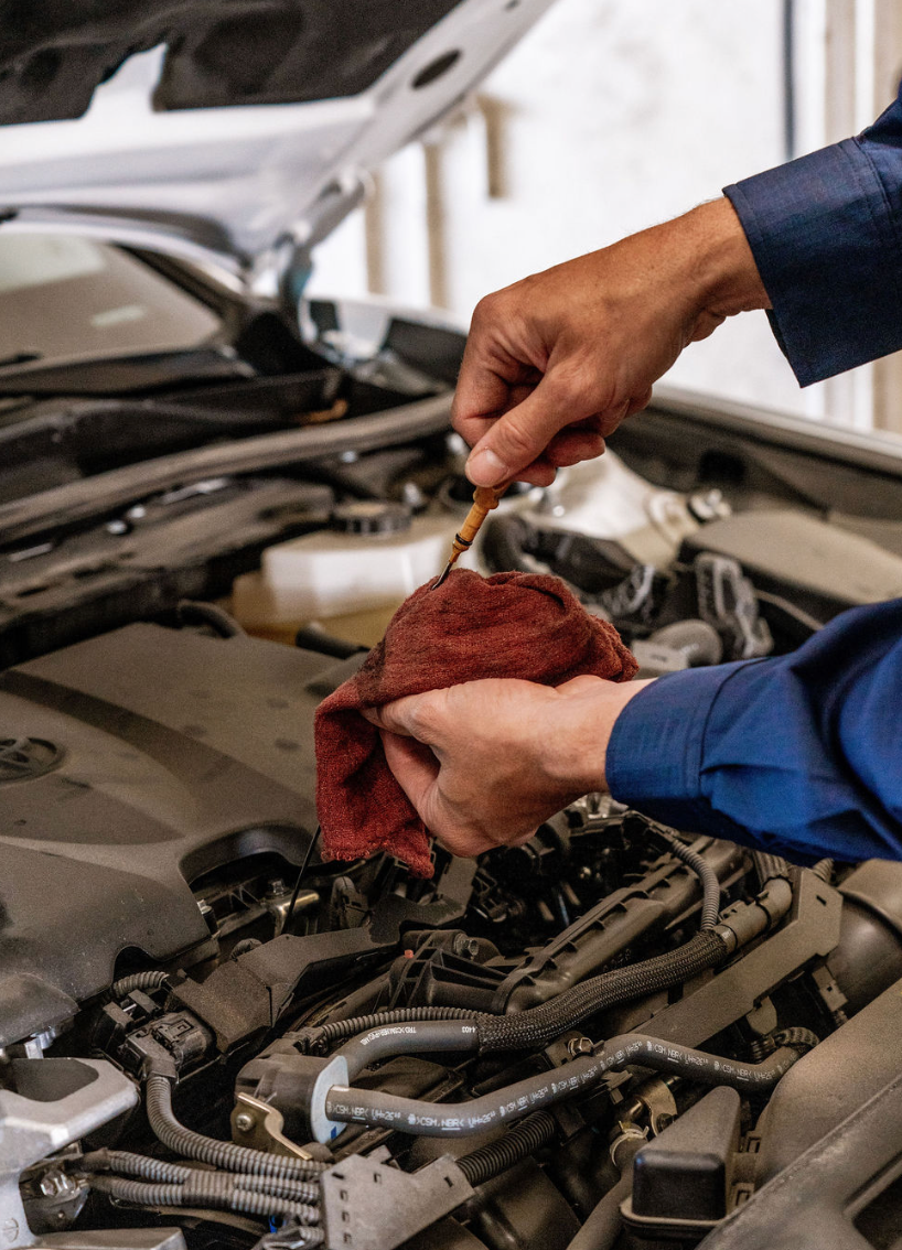 Mechanic wiping engine parts with a red cloth under a car hood