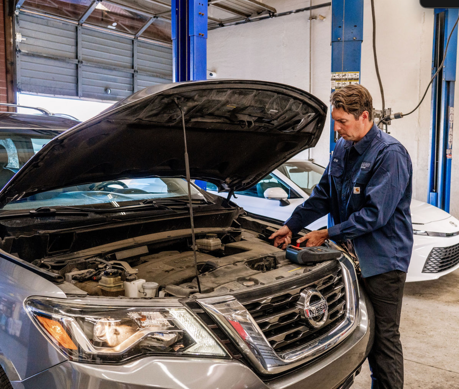 Mechanic working on a silver SUV with hood open in a garage