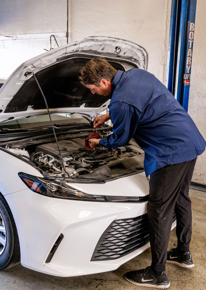 Mechanic in blue shirt working under the hood of a white car in a garage