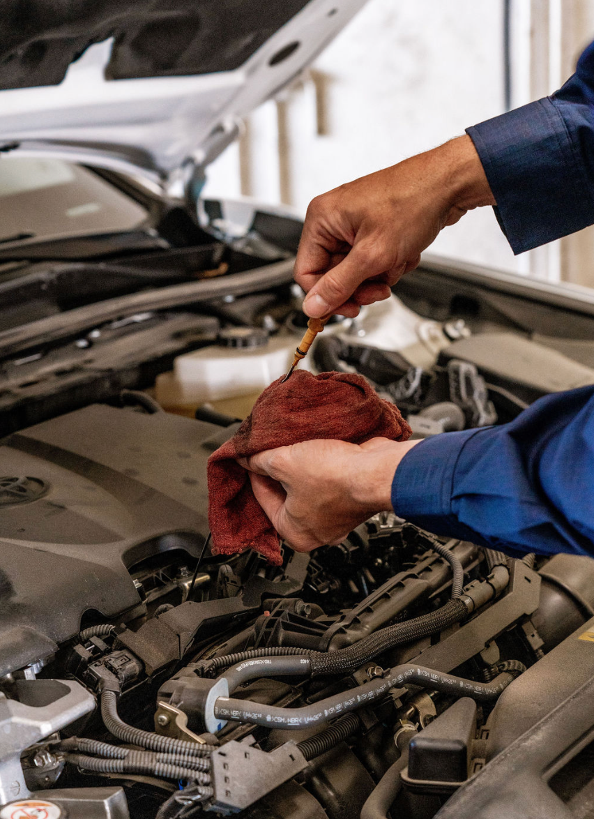Mechanic using a red rag to check engine oil under an open car hood