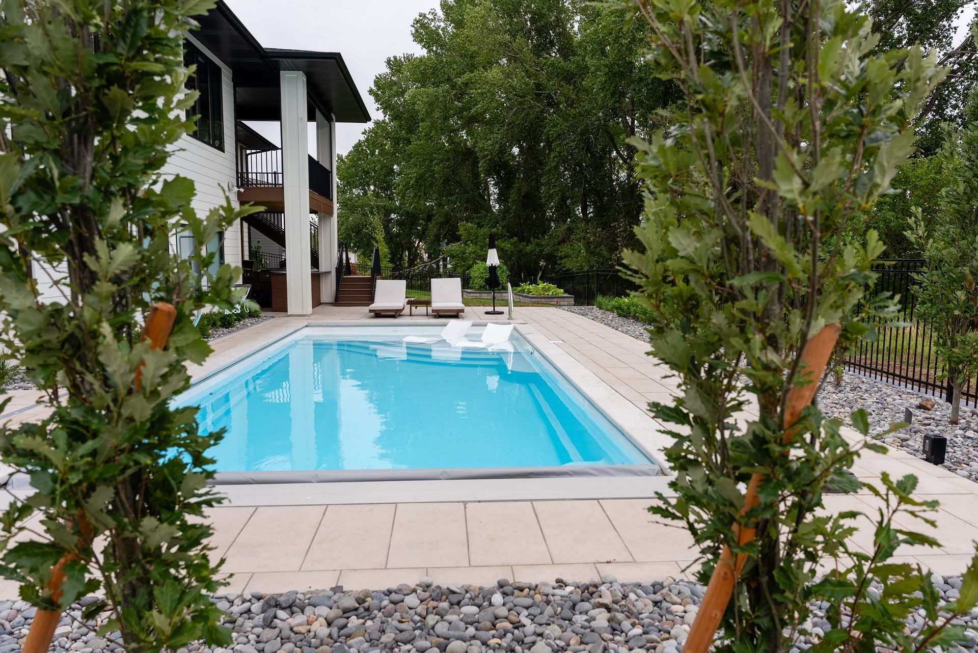 A rectangular swimming pool surrounded by a stone patio, with a house in the background.