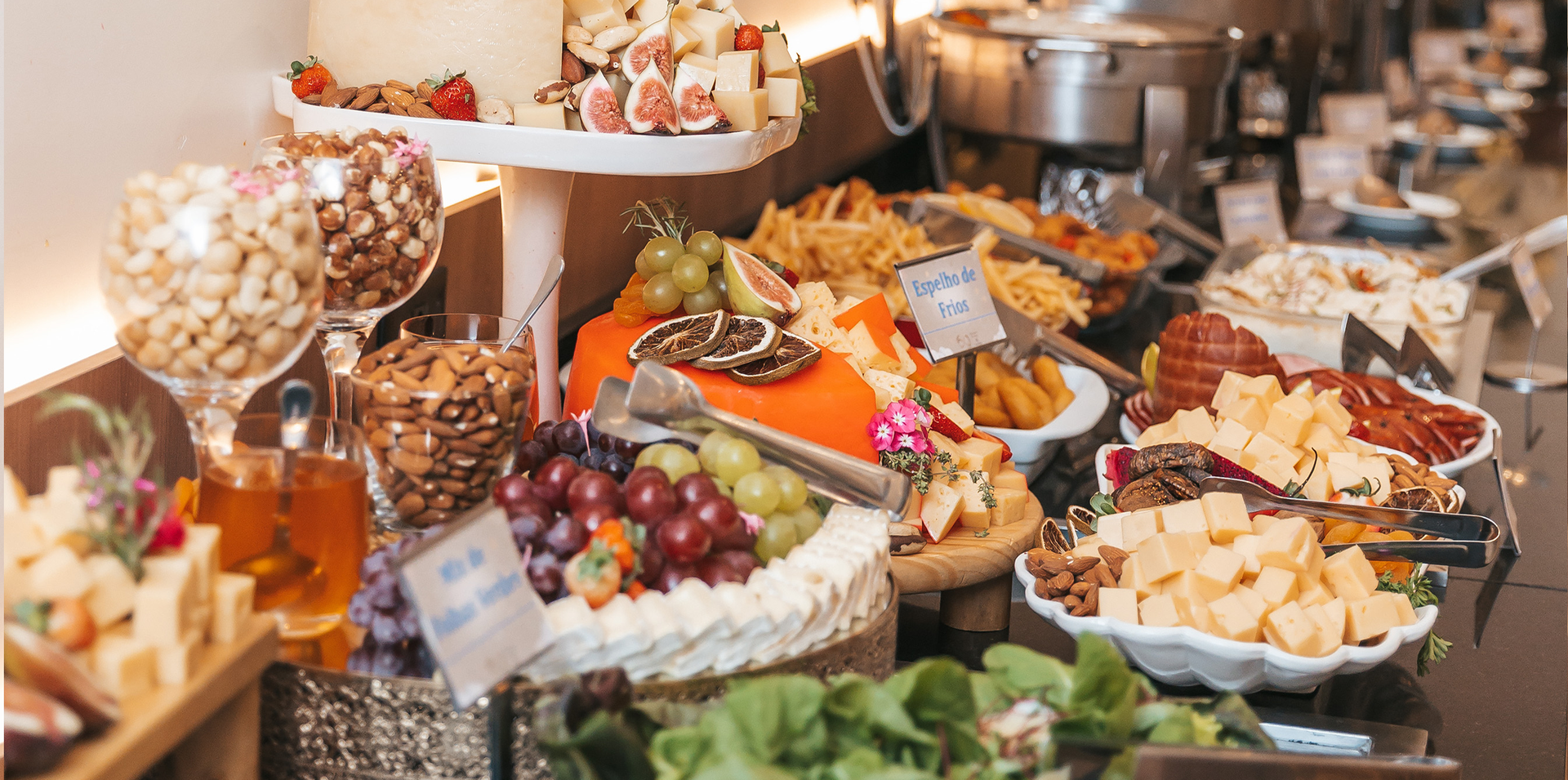 Mesa de bufê com frutas variadas, sobremesas e aperitivos em travessas e tigelas.